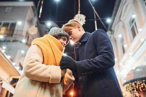 proximidade das pessoas. casal jovem feliz em roupas quentes está na rua decorada de Natal juntos foto