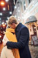 jovem casal em roupas quentes beijando na rua decorada de natal foto