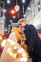 jovem casal em roupas quentes beijando na rua decorada de natal foto