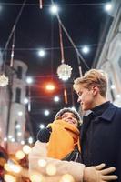 casal jovem feliz em roupas quentes está na rua decorada de Natal juntos foto