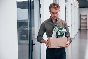 trabalhador de escritório com roupa formal andando com caixa com planta verde dentro dela foto