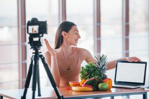 jovem vlogger fitness fazendo vídeo dentro de casa sentado perto da mesa com comida saudável foto