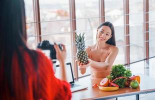 modelo fitness tem sessão de fotos de fotógrafa dentro de casa perto da mesa com comida saudável