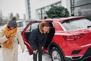 jovem casal dançando perto de carro com árvore no topo. juntos ao ar livre no inverno foto