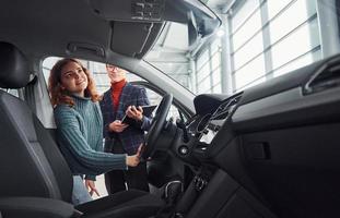 vendedor profissional ajudando jovem escolhendo novo automóvel moderno dentro de casa foto