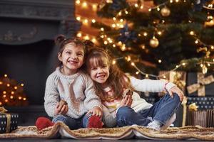 duas meninas se divertem na sala decorada de natal com caixas de presente foto