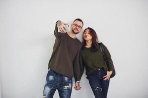 alegre casal multiétnico em roupas casuais fazendo selfie dentro de casa no estúdio contra fundo branco foto