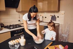 mãe com sua filha preparando comida na cozinha e se divertir foto