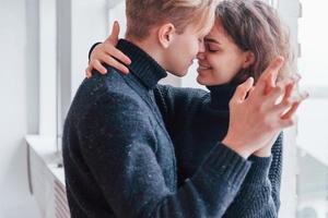 casal jovem bonito se abraçando dentro de casa perto da janela foto