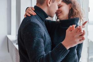 casal jovem bonito se abraçando dentro de casa perto da janela foto