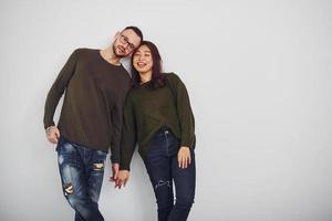 feliz casal multiétnico em roupas casuais está junto dentro de casa no estúdio. cara caucasiano com namorada asiática foto