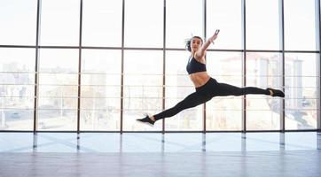 jovem mulher desportiva em roupas esportivas pulando e fazendo truques atléticos contra a janela no ar