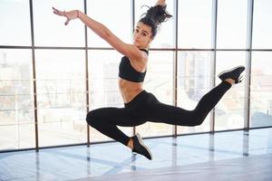 jovem mulher desportiva em roupas esportivas pulando e fazendo truques atléticos contra a janela no ar foto