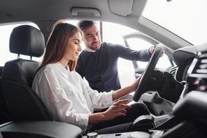 mulher testando carro com ajuda de assistente masculino dentro de casa no salão foto