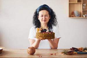 mulher sênior com cabelo encaracolado preto segurando bolo dietético na cozinha foto