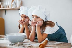 duas meninas em uniforme de chef azul sorrindo juntas na cozinha foto