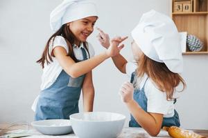 duas meninas em uniforme de chef azul se divertem com farinha na cozinha foto