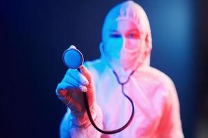 enfermeira com máscara e uniforme branco e com estetoscópio em pé na sala iluminada por neon foto