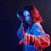 retrato de jovem ouvindo música em fones de ouvido em néon vermelho e azul no estúdio foto
