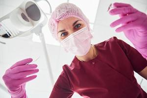 jovem dentista feminina em máscara protetora trabalhando na clínica de estomatologia. visão em primeira pessoa foto