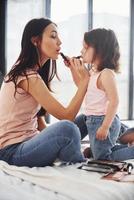 aprendendo a se maquiar. jovem mãe com a filha passando o fim de semana juntos no quarto foto