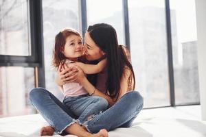 jovem mãe com sua filha se abraçando na cama foto