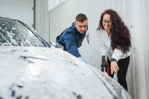 cliente do sexo feminino falando o que fazer. trabalhador masculino de uniforme lavando carro novo e moderno dentro de casa. concepção de serviço foto