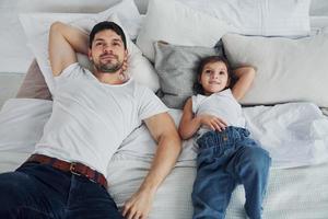 pai feliz com sua filha passando tempo livre em casa juntos. deitado na cama foto