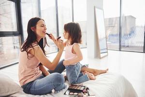 aprendendo a se maquiar. jovem mãe com a filha passando o fim de semana juntos no quarto foto