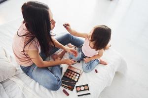 aprendendo a se maquiar. jovem mãe com a filha passando o fim de semana juntos no quarto foto