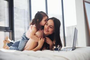 jovem mãe com a filha passando o fim de semana juntos no quarto e usando o laptop foto
