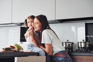 mãe com sua filhinha se abraçando dentro de casa na cozinha foto