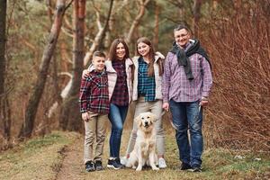 família feliz em pé junto com seu cachorro ao ar livre na floresta foto