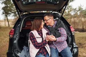 casal maduro feliz sentado na parte de trás de um carro ao ar livre na floresta foto