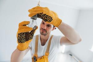 faz-tudo em uniforme amarelo trocando a lâmpada. concepção de renovação de casa foto