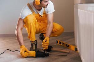 faz-tudo em uniforme amarelo trabalha dentro de casa usando furadeira de martelo. concepção de renovação de casa foto