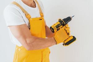 faz-tudo em uniforme amarelo em pé contra a parede branca com chave de fenda automática. concepção de renovação de casa foto