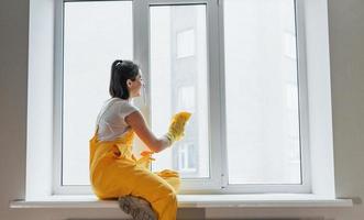 dona de casa de uniforme amarelo limpando janelas. concepção de renovação de casa foto