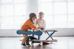 dois meninos em uniforme de piloto retrô se divertindo com avião de brinquedo dentro de casa foto