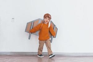 menino em uniforme de piloto retrô correndo com avião de brinquedo dentro de casa foto