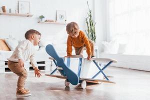 dois meninos em uniforme de piloto retrô se divertindo com avião de brinquedo dentro de casa foto