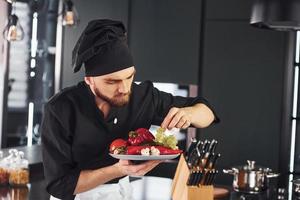 Com vegetais. cozinheiro profissional jovem chef de uniforme trabalhando na cozinha foto