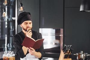 cozinheiro profissional jovem chef de uniforme em pé com o bloco de notas na cozinha foto
