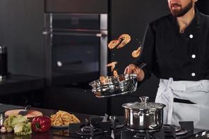 cozinheiro profissional jovem chef de uniforme fritando alimentos na cozinha foto