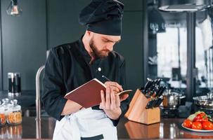 cozinheiro profissional jovem chef de uniforme em pé com o bloco de notas na cozinha foto