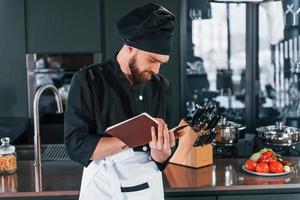 cozinheiro profissional jovem chef de uniforme em pé com o bloco de notas na cozinha foto