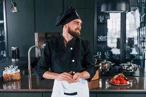 retrato de cozinheiro profissional jovem chef de uniforme que posando para a câmera na cozinha foto