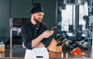 cozinheiro profissional jovem chef de uniforme em pé com o telefone na cozinha foto
