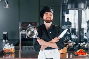 retrato de cozinheiro profissional jovem chef de uniforme que posando para a câmera na cozinha foto