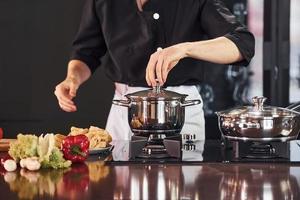 usando equipamentos. cozinheiro profissional jovem chef de uniforme trabalhando na cozinha com legumes foto